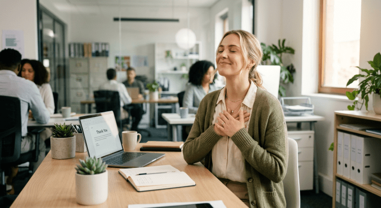 Woman sitting at desk with eyes closed and hands on chest expressing gratitude